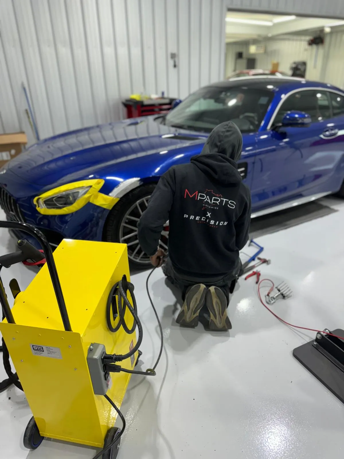 Technician performing structural repair on a blue Mercedes-AMG GT