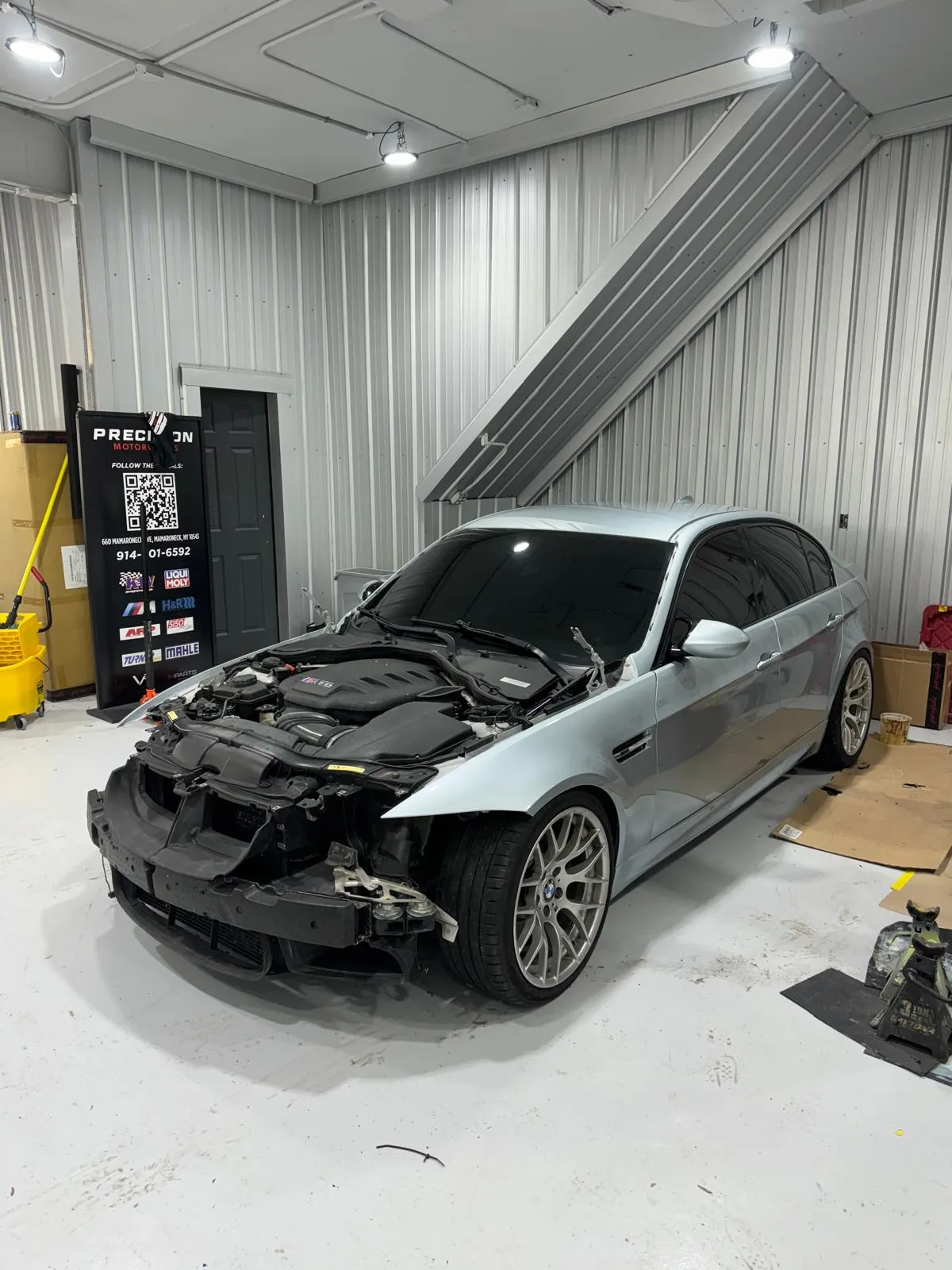 Silver E90 M3 front-end teardown for collision repair. S65 V8 exposed during disassembly process.